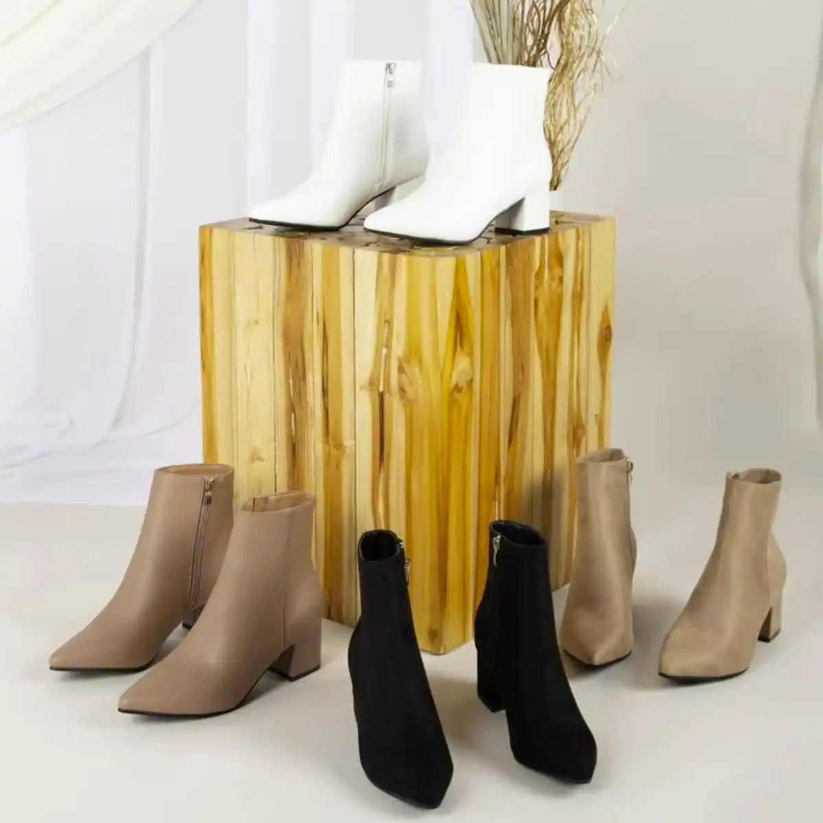 Collection of ankle boots in beige, black, and white colors arranged around a gold-toned pedestal.