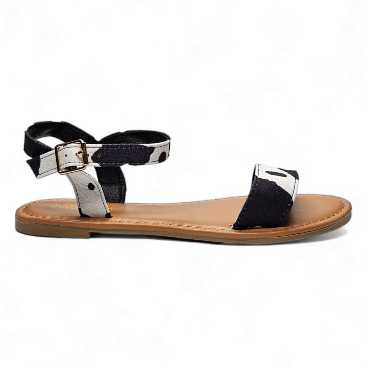 Flat cow print sandal with black straps and a silver buckle on a tan sole