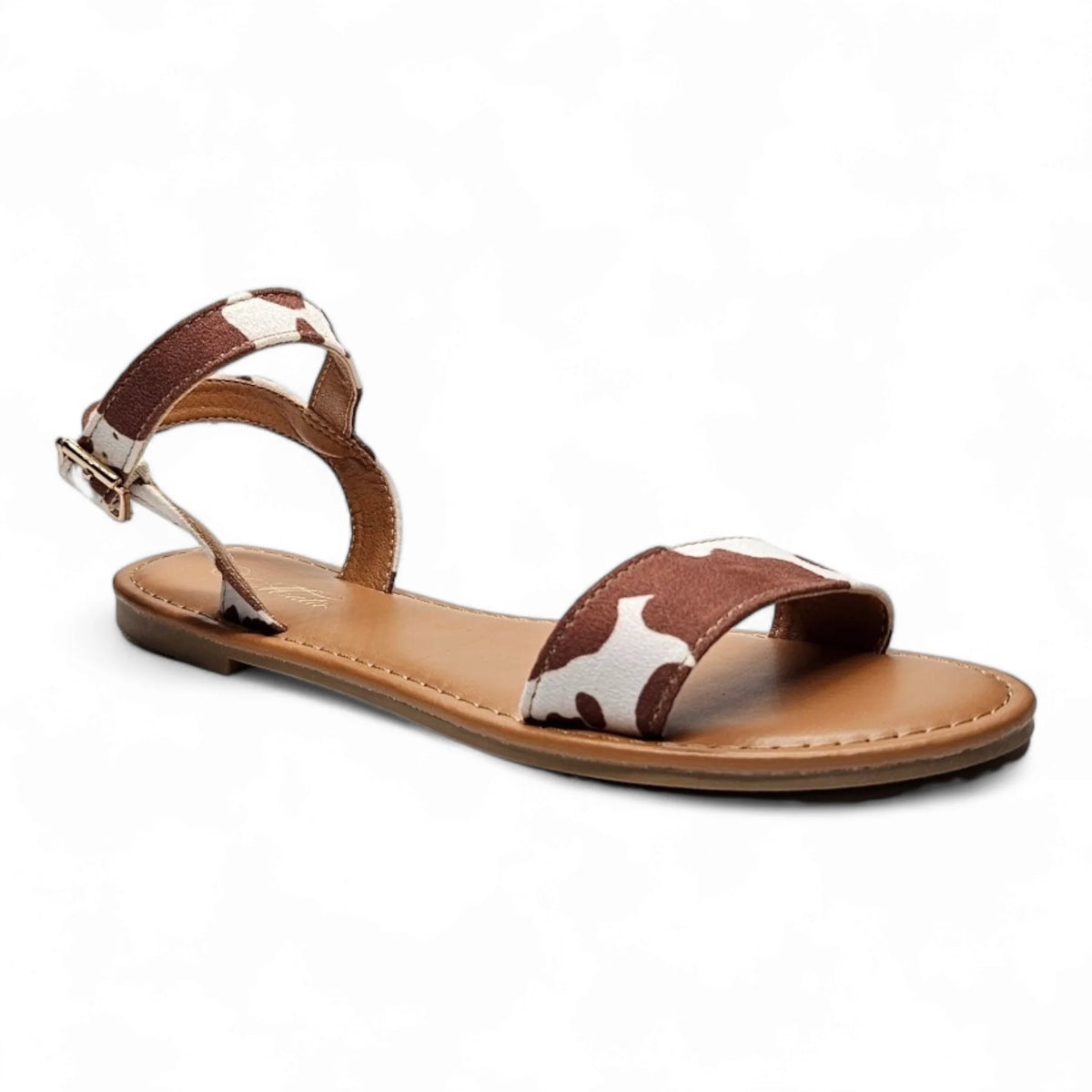 Flat sandal featuring brown and white cow print straps with buckle closure