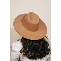 Tan flat brim fedora hat worn by a person with dark curly hair