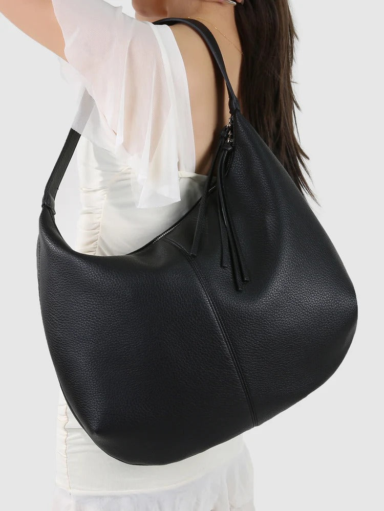 Black leather handbag worn by a person on a white background