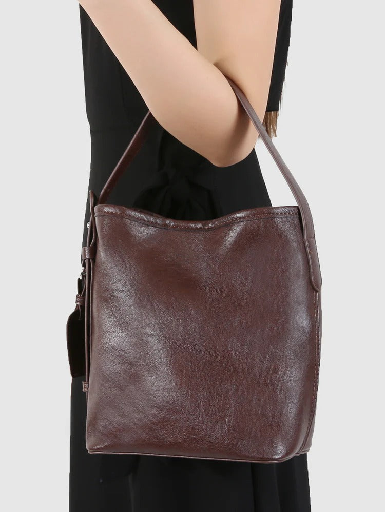 Brown leather shoulder bag worn by a person on a light gray background