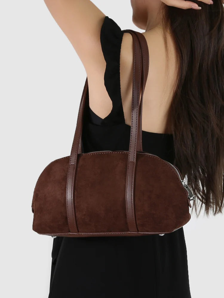 Brown handbag held by a person wearing a black dress on a white background
