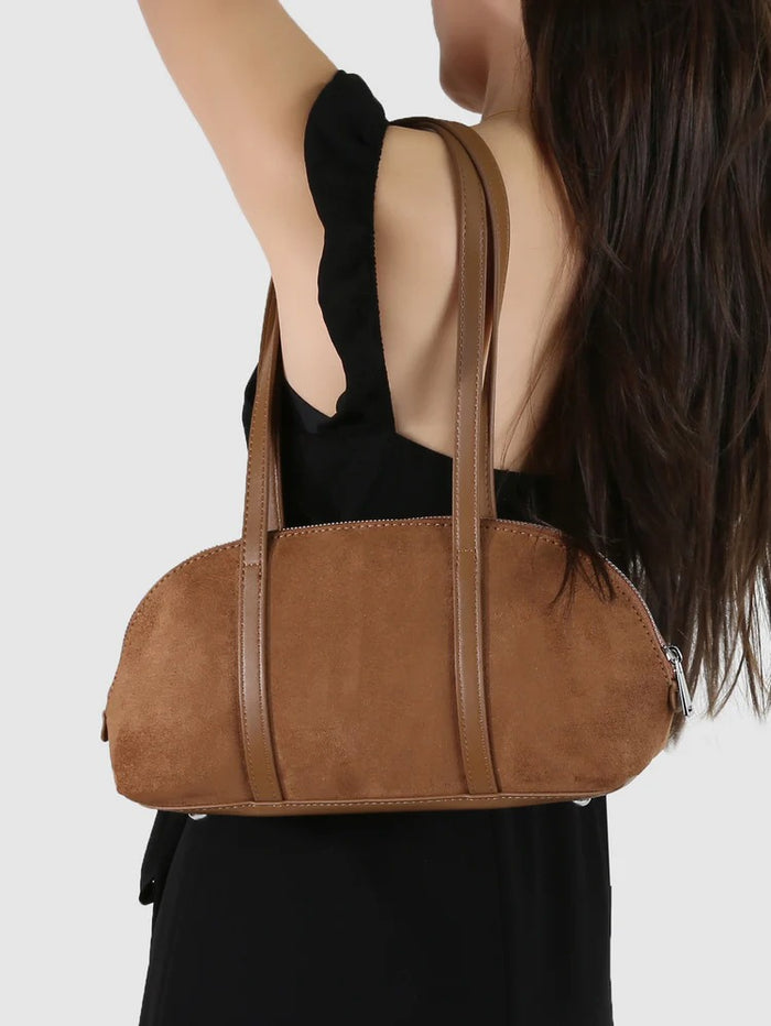 Brown handbag held by a person against a white background