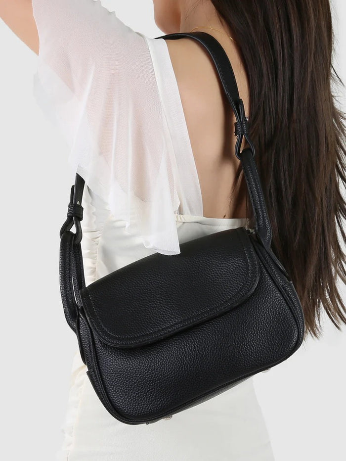 Black leather handbag worn by a person on a white background