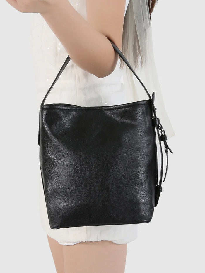 Black leather handbag held by a person on a white background