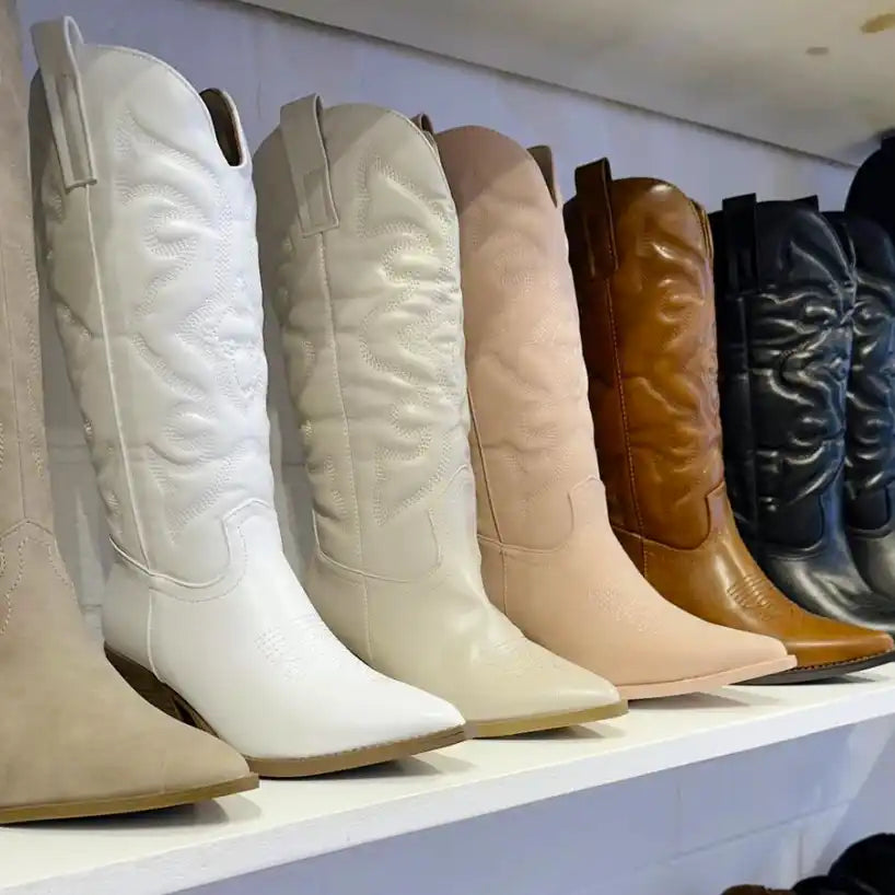 Row of western-style cowboy boots in different neutral colors ranging from white to brown to black.