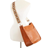 Tan leather crossbody bag featuring a decorative woven guitar strap for stylish carry