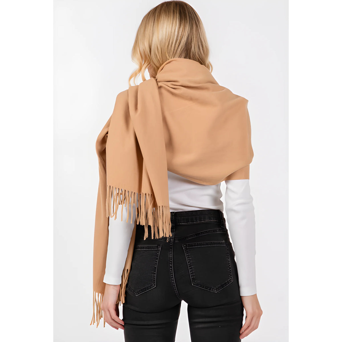 Camel-colored fringed oblong scarf draped over shoulders with white top and dark jeans