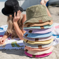 Stack of colorful Terry Cloth Bucket Hats on a beach towel for summer fun