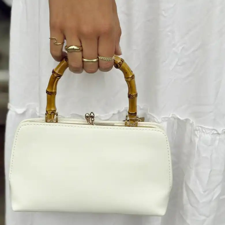 White handbag with bamboo handles and gold-tone frame closure.